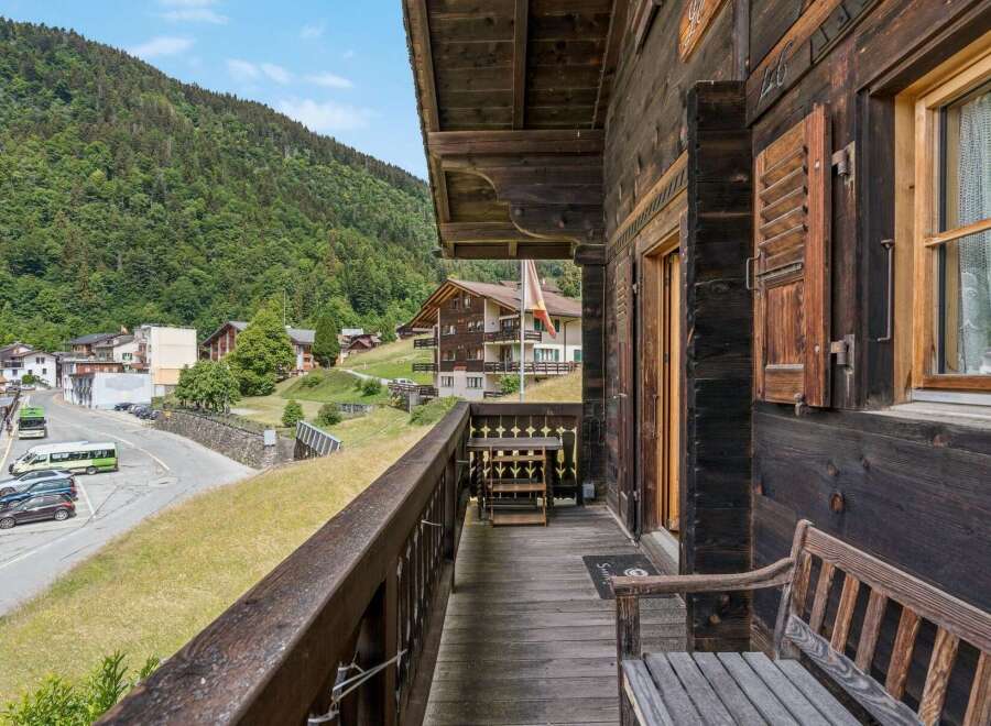 Experience the charm of alpine living with this rustic wooden balcony offering stunning views of a lush green mountainside and a quaint village.