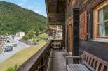 Experience the charm of alpine living with this rustic wooden balcony offering stunning views of a lush green mountainside and a quaint village.