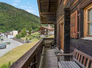 Experience the charm of alpine living with this rustic wooden balcony offering stunning views of a lush green mountainside and a quaint village.
