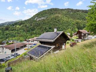 Experience sustainable living in this charming alpine home, featuring a prominent solar panel installation on its roof, perfect for eco-conscious buyers.