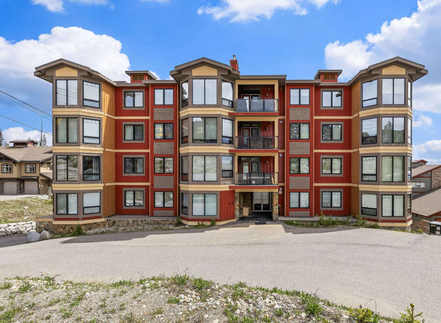 Experience luxury mountain living in this stunning condo complex, featuring a vibrant red and tan exterior with expansive windows offering breathtaking views.