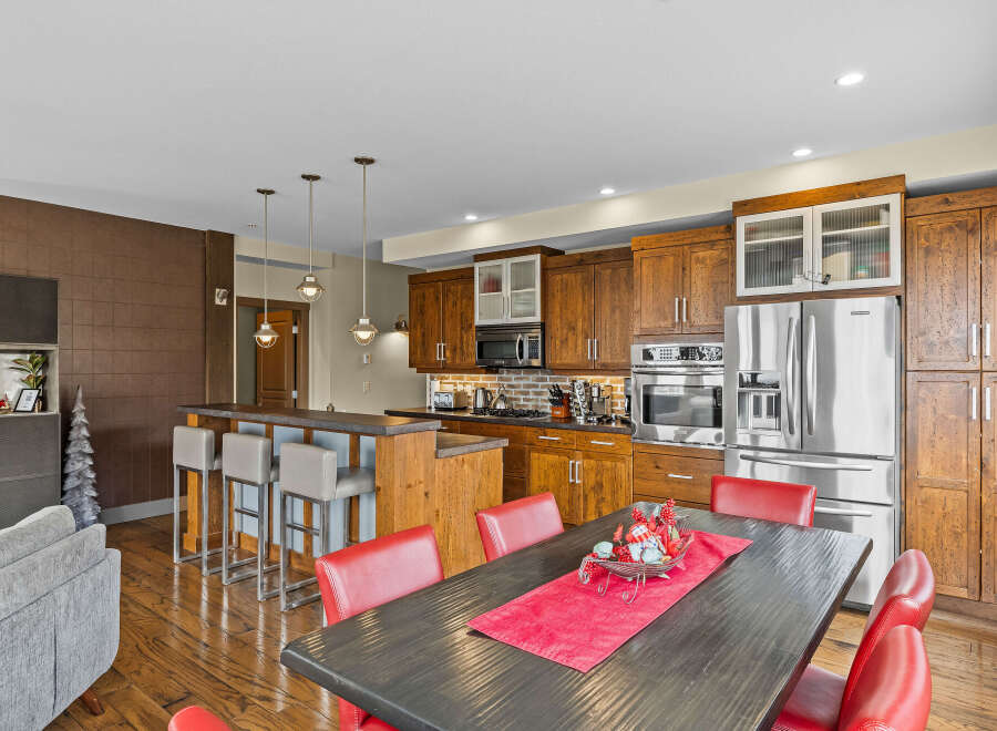 This spacious kitchen boasts rich wooden cabinetry, a large stainless steel refrigerator, and a breakfast bar with comfortable seating.