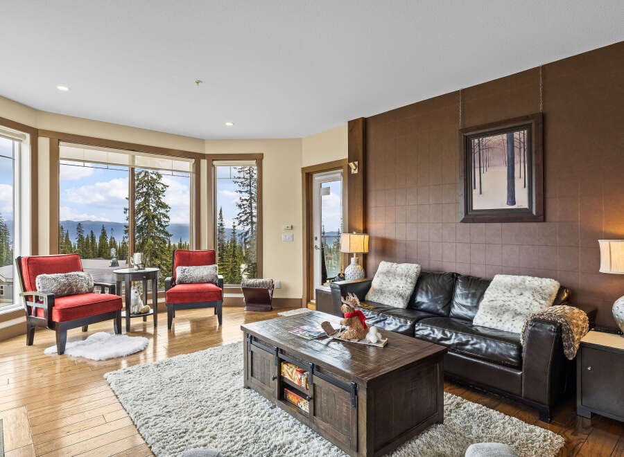 Experience breathtaking mountain views from this stunning living room, featuring a cozy leather sofa and two accent chairs perfect for relaxing.