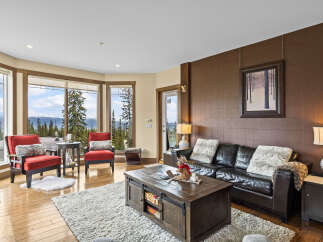 Experience breathtaking mountain views from this stunning living room, featuring a cozy leather sofa and two accent chairs perfect for relaxing.
