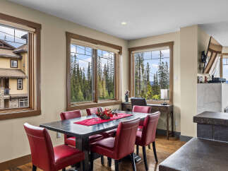 Experience breathtaking mountain views from this elegant dining area, featuring a spacious dark wood table surrounded by plush red chairs.