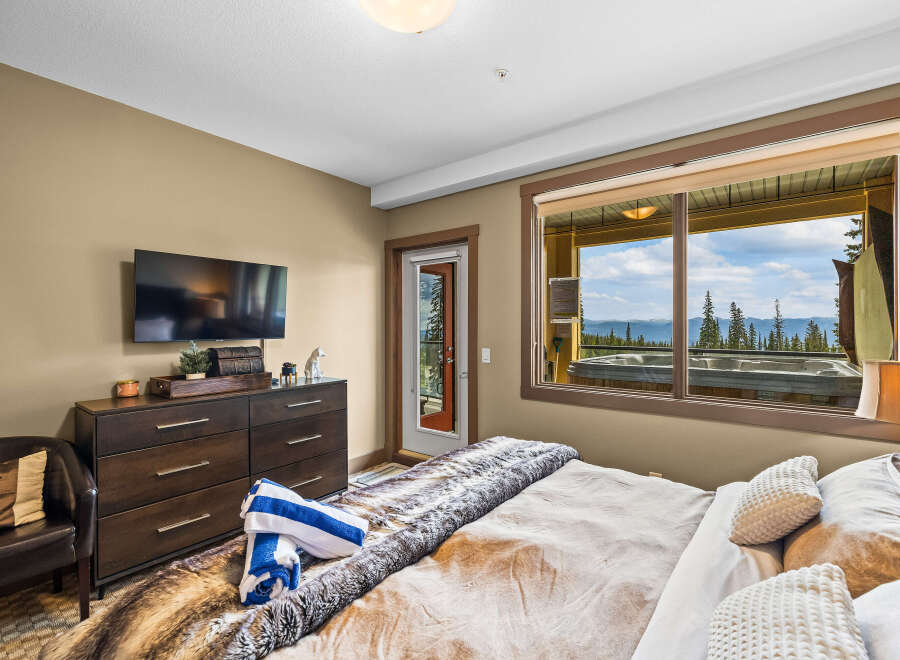 Experience ultimate relaxation in this luxurious bedroom, featuring a plush fur throw and a private balcony with a hot tub overlooking a stunning mountain vista.