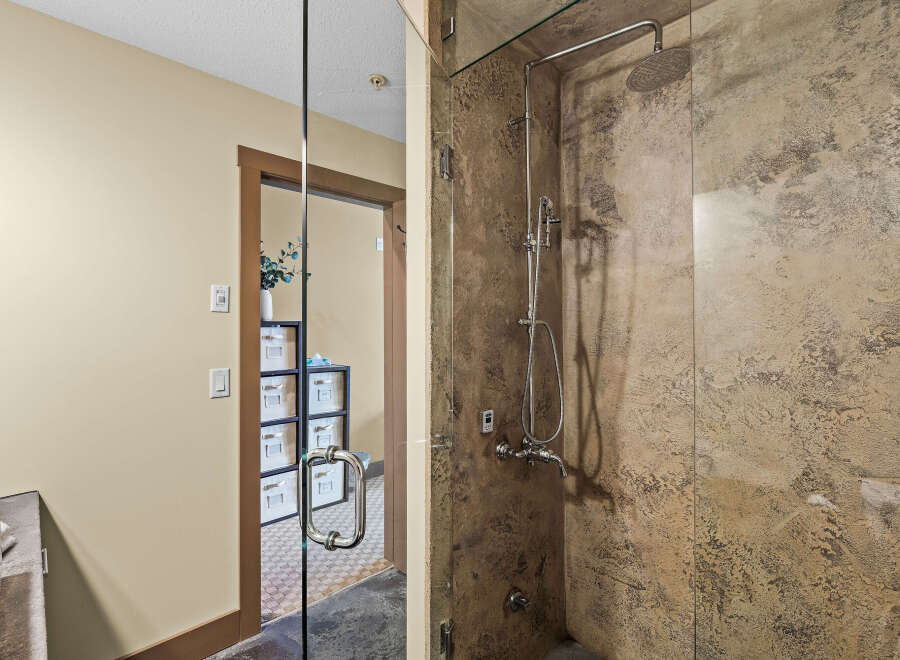Experience luxury in this modern bathroom featuring a spacious walk-in shower with a rainfall showerhead and a sleek, textured stone finish.