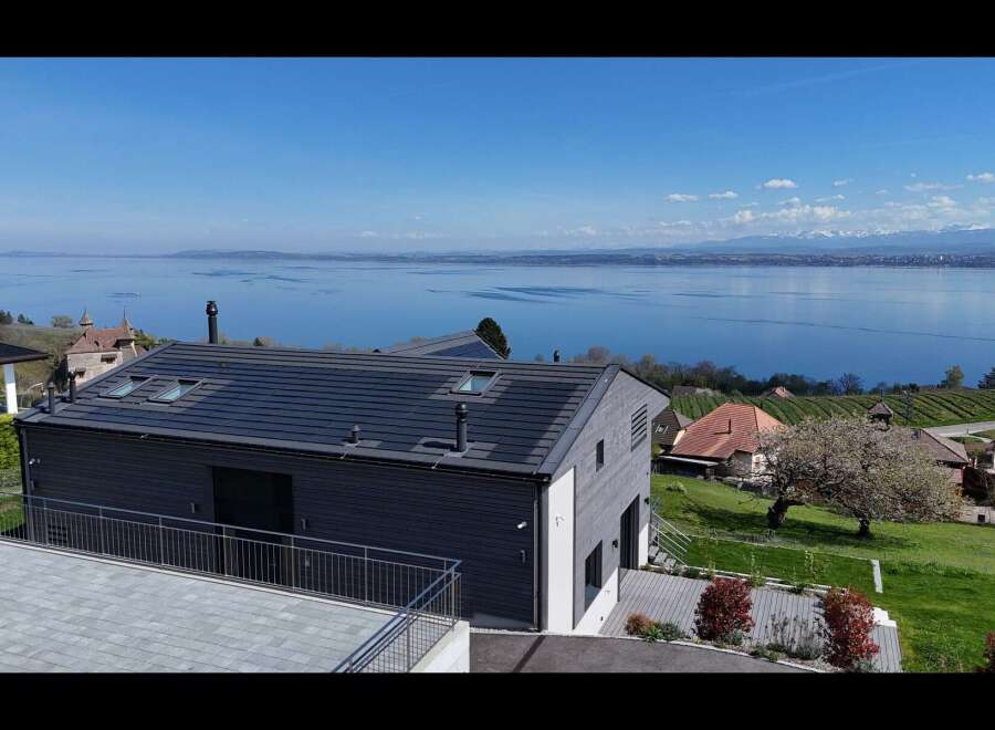 Experience breathtaking lake and mountain views from this modern home, featuring a sleek dark-tiled roof and expansive windows.