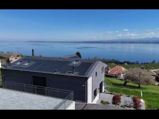 Experience breathtaking lake and mountain views from this modern home, featuring a sleek dark-tiled roof and expansive windows.
