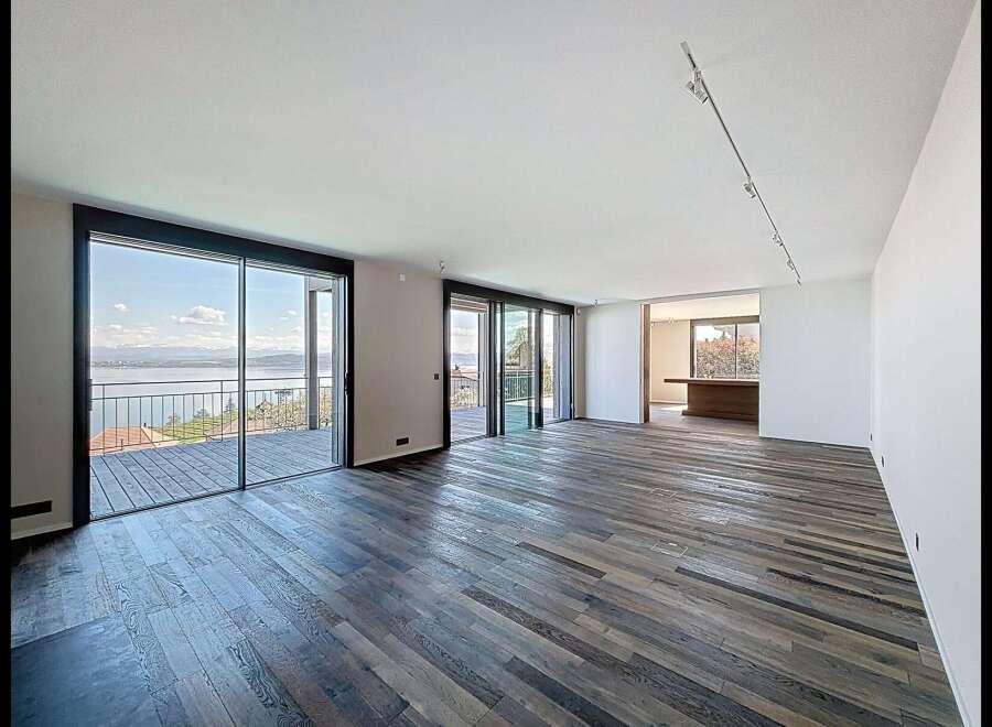 Experience breathtaking lake and mountain views from this spacious living area, featuring expansive floor-to-ceiling windows that open onto a private deck.