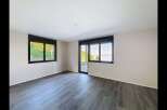Experience modern living in this spacious room featuring large windows that offer stunning views of a lush green hillside and a serene lake.