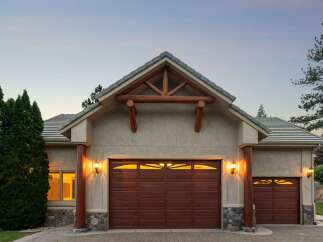Experience rustic charm with this stunning home featuring a prominent wooden truss gable above a rich brown garage door.