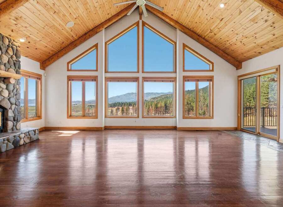 Experience breathtaking mountain views from this stunning living room, featuring a grand stone fireplace and soaring vaulted ceilings with exposed wooden beams.