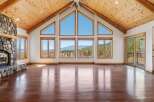 Experience breathtaking mountain views from this stunning living room, featuring a grand stone fireplace and soaring vaulted ceilings with exposed wooden beams.