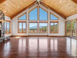 Experience breathtaking mountain views from this stunning living room, featuring a grand stone fireplace and soaring vaulted ceilings with exposed wooden beams.
