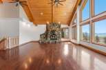 Experience breathtaking lake and mountain views from this stunning living room, featuring a grand stone fireplace and soaring vaulted ceilings with exposed wooden beams.