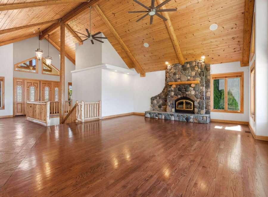 Experience rustic charm in this spacious living area featuring a grand stone fireplace and soaring vaulted ceilings with exposed wooden beams.