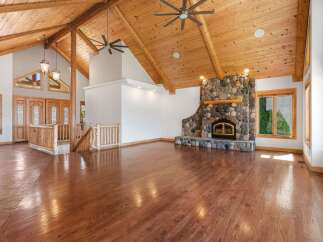Experience rustic charm in this spacious living area featuring a grand stone fireplace and soaring vaulted ceilings with exposed wooden beams.