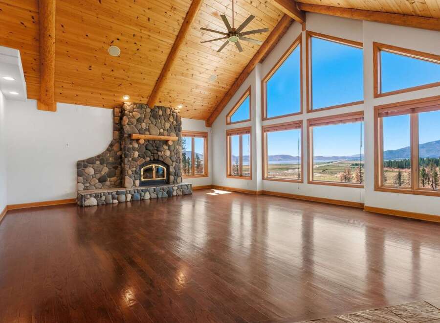 Experience breathtaking panoramic views from this stunning living room, featuring a grand stone fireplace and soaring vaulted ceilings with exposed wood beams.