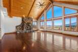 Experience breathtaking panoramic views from this stunning living room, featuring a grand stone fireplace and soaring vaulted ceilings with exposed wood beams.