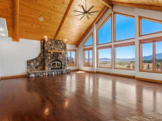 Experience breathtaking panoramic views from this stunning living room, featuring a grand stone fireplace and soaring vaulted ceilings with exposed wood beams.