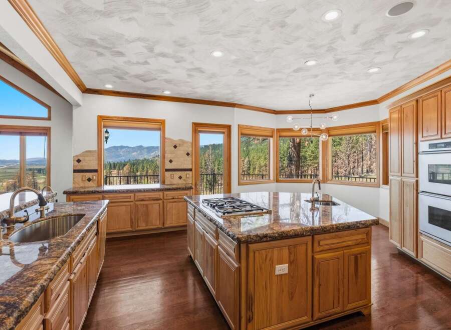 Experience breathtaking mountain views from this stunning kitchen, featuring a large granite island with a gas stovetop and a double sink.