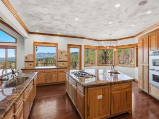Experience breathtaking mountain views from this stunning kitchen, featuring a large granite island with a gas stovetop and a double sink.