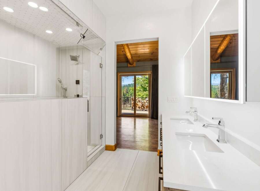 Experience luxury in this modern bathroom featuring a spacious glass-enclosed shower and a sleek double vanity with illuminated mirrors.