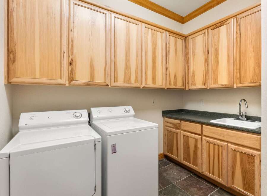 This laundry room features ample storage with light wood cabinetry above and below the countertop.