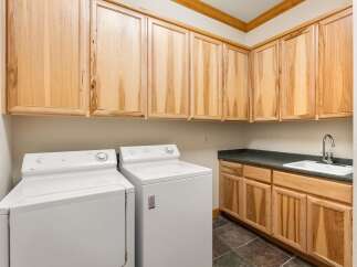 This laundry room features ample storage with light wood cabinetry above and below the countertop.