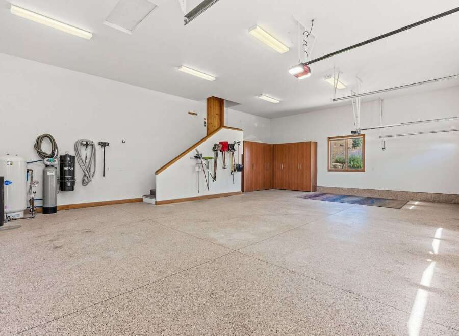 This spacious garage offers ample storage with built-in wooden cabinets and a dedicated area for tools, including shovels, rakes, and brooms.