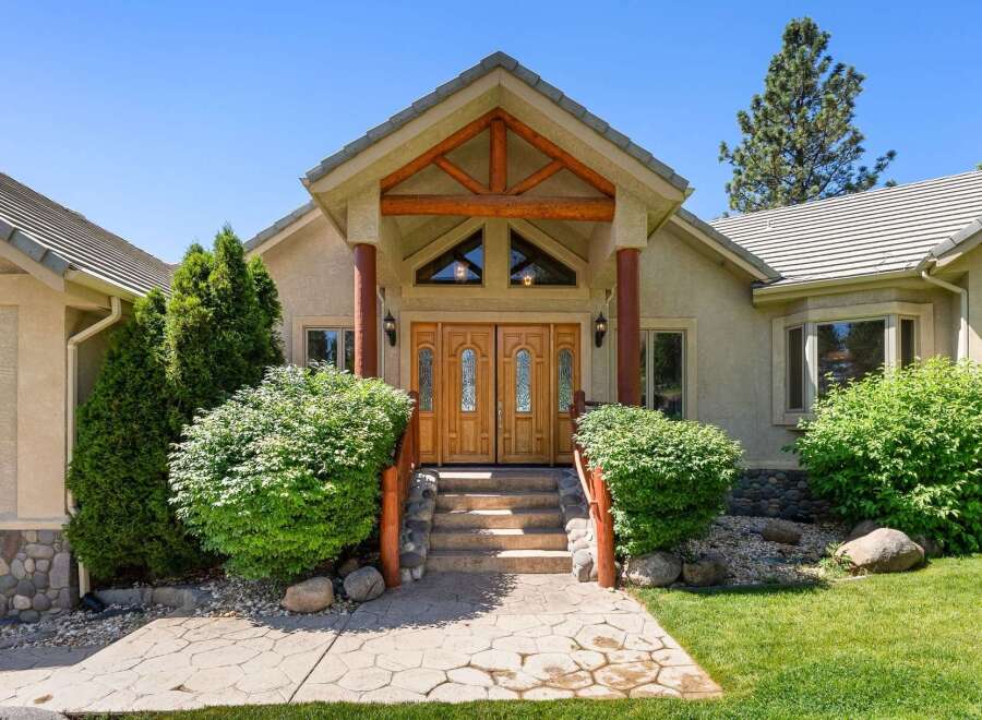 This stunning home features a grand entrance with double wooden doors and a covered porch supported by rustic wooden beams and columns.