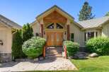 This stunning home features a grand entrance with double wooden doors and a covered porch supported by rustic wooden beams and columns.