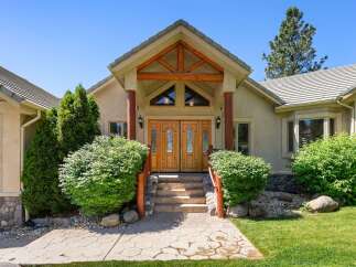 This stunning home features a grand entrance with double wooden doors and a covered porch supported by rustic wooden beams and columns.