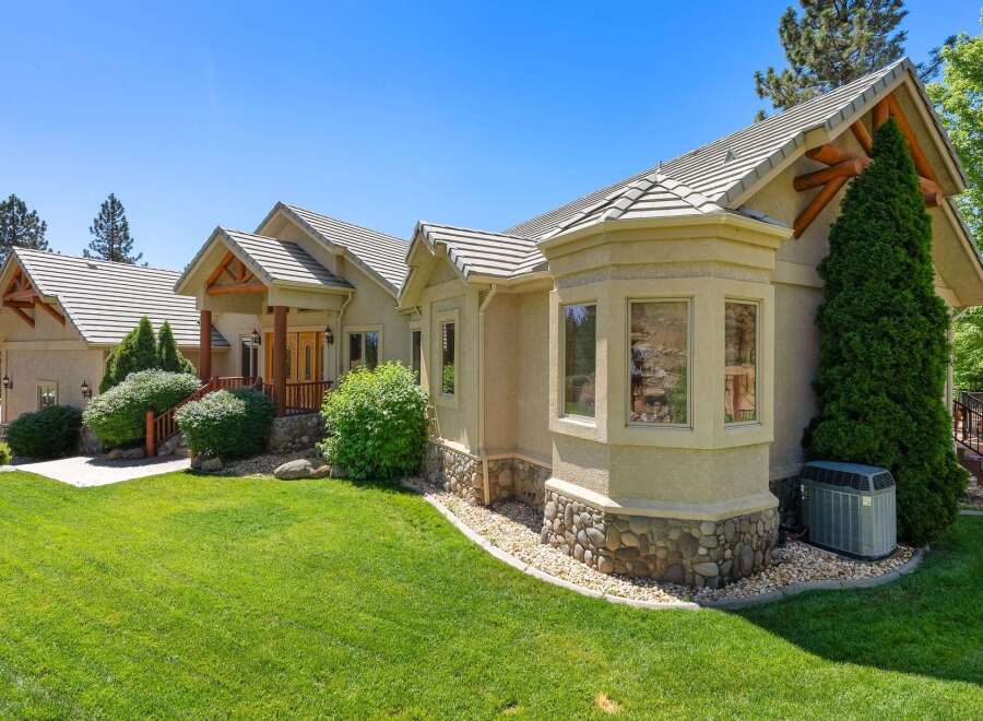 This stunning home features a beautiful stucco exterior with a stone accent base, complemented by a multi-level roofline and exposed wooden beams.