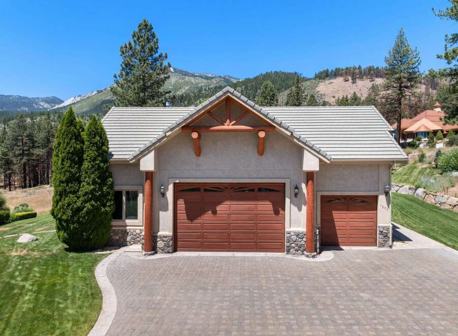 This stunning property features a spacious three-car garage with beautiful wood doors and stone accents, perfect for housing vehicles and storage.