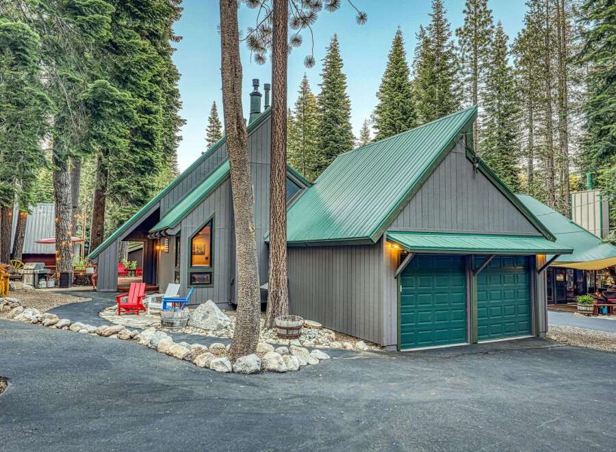 Nestled amidst towering pine trees, this charming mountain home boasts a striking A-frame design with a durable green metal roof.