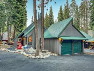 Nestled amidst towering pine trees, this charming mountain home boasts a striking A-frame design with a durable green metal roof.