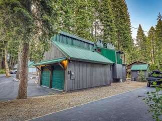 Nestled amidst towering pine trees, this unique property features a striking modern cabin with a vibrant green metal roof and complementary siding.