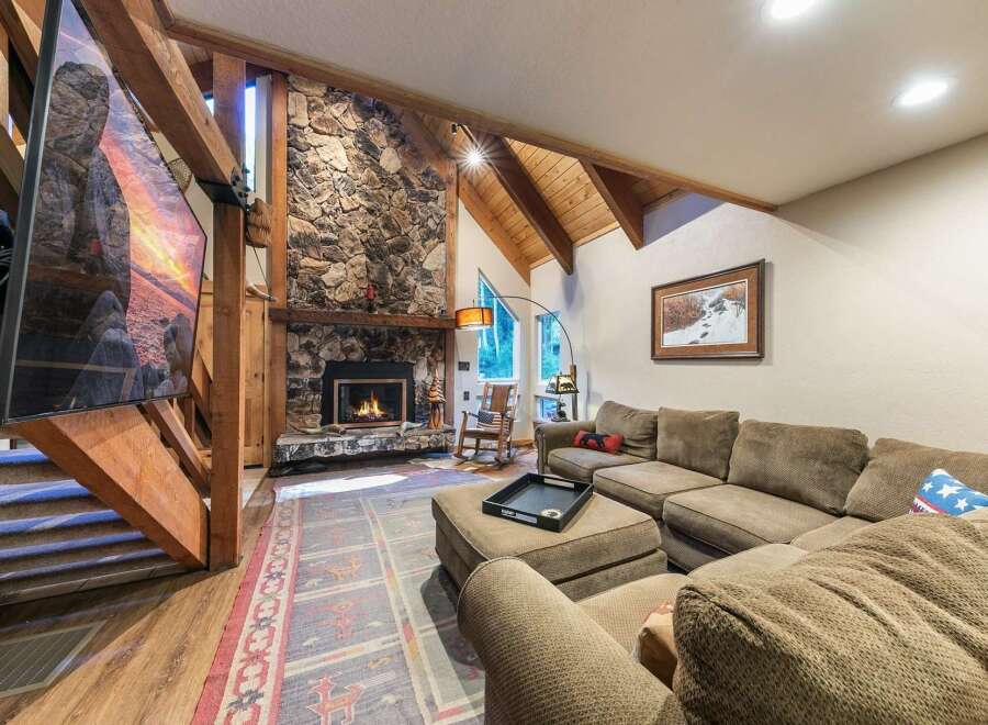 Experience rustic charm in this spacious living room, featuring a grand stone fireplace and exposed wooden beams that create a warm, inviting atmosphere.
