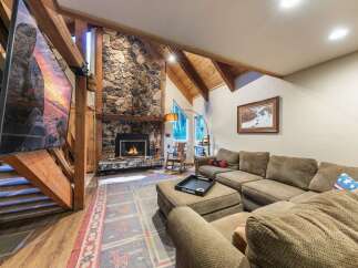 Experience rustic charm in this spacious living room, featuring a grand stone fireplace and exposed wooden beams that create a warm, inviting atmosphere.