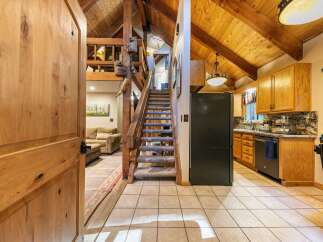 Step into this charming cabin-style home featuring a grand wooden door that opens to a spacious living area and a well-equipped kitchen.