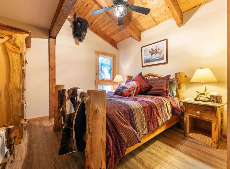 Experience rustic charm in this cozy bedroom, featuring a unique log bed adorned with a striking striped comforter and a plush cowhide throw.
