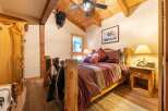Experience rustic charm in this cozy bedroom, featuring a unique log bed adorned with a striking striped comforter and a plush cowhide throw.