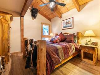 Experience rustic charm in this cozy bedroom, featuring a unique log bed adorned with a striking striped comforter and a plush cowhide throw.