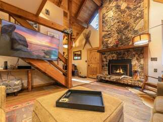Experience rustic charm in this inviting living room, featuring a grand stone fireplace and exposed wooden beams that create a cozy, lodge-like atmosphere.