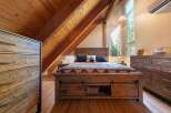 Experience rustic charm in this cozy bedroom, featuring a wooden plank headboard and a unique sliding barn door storage system under the bed.