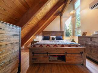 Experience rustic charm in this cozy bedroom, featuring a wooden plank headboard and a unique sliding barn door storage system under the bed.