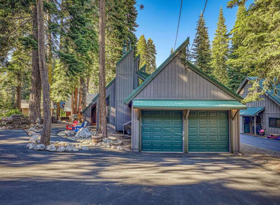 Nestled among tall pine trees, this charming property features a striking modern A-frame home with a distinctive green metal roof and a spacious two-car garage.