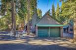 Nestled among tall pine trees, this charming property features a striking modern A-frame home with a distinctive green metal roof and a spacious two-car garage.